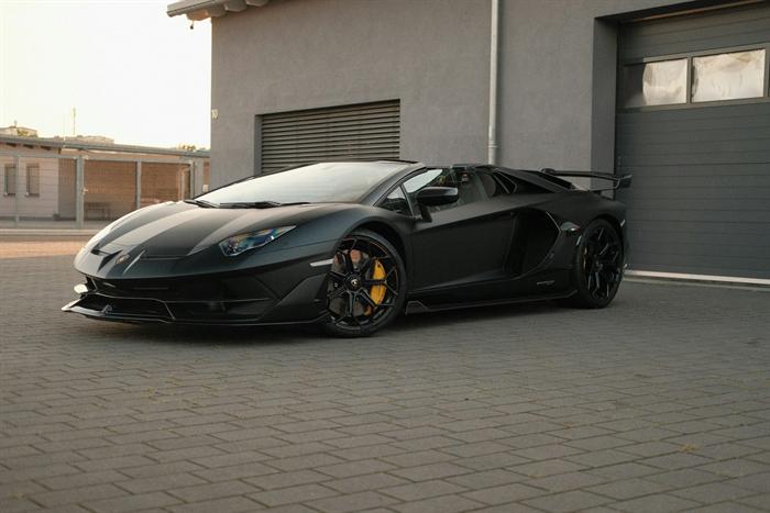 Black supercar with gold wheels parked in front of a garage