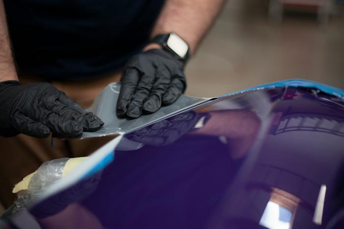 Technician in black gloves working on a deep purple painted panel