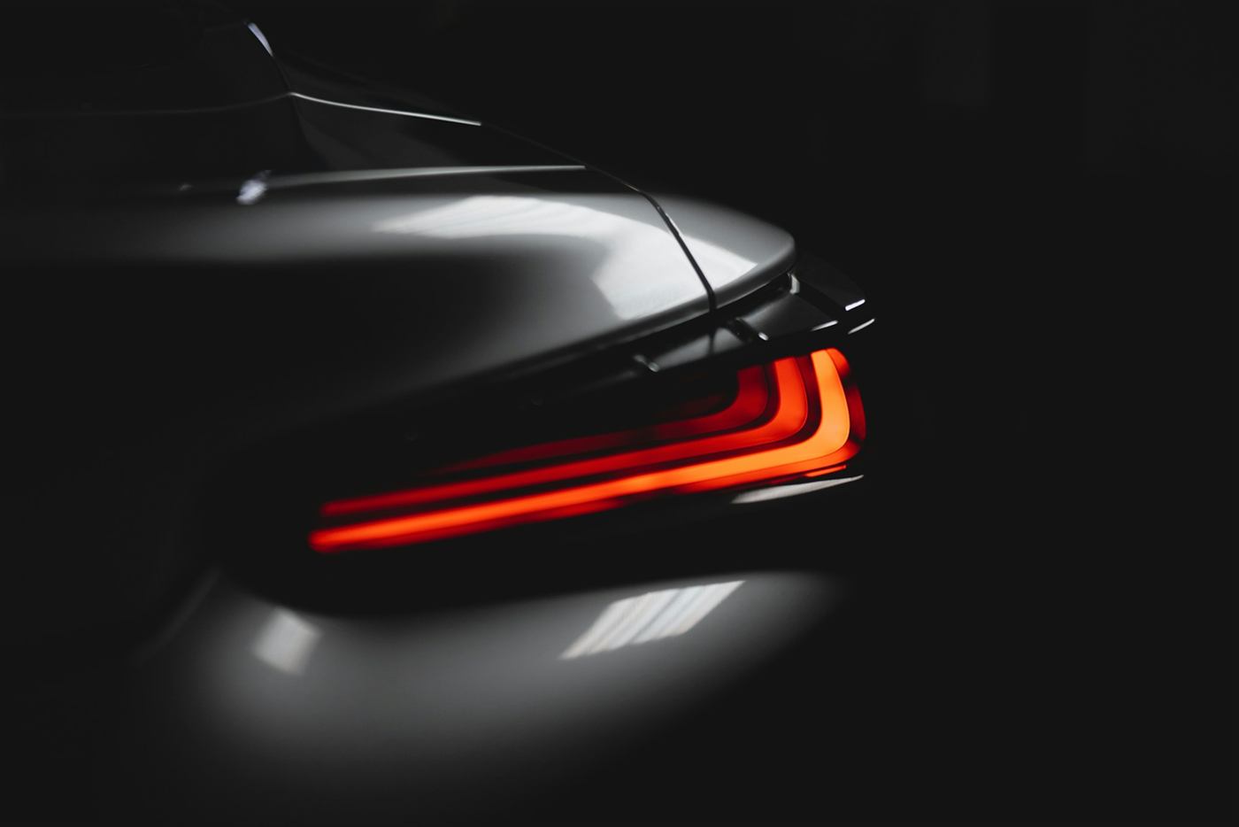 Rear light signature of a black performance car glowing red in a dark studio