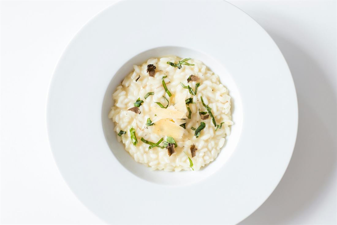 Wild mushroom risotto with shaved parmesan and herbs in a white bowl