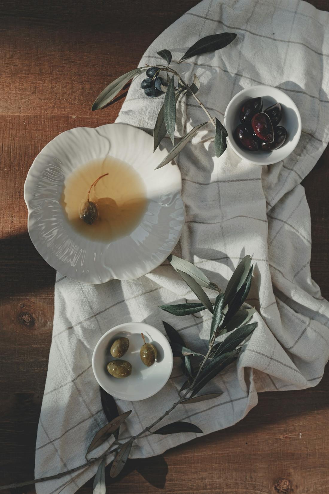 Green and black olives in white bowls with olive branches on a checked linen cloth
