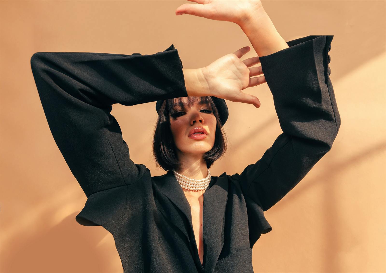 Model in a black blazer with raised hands against a peach wall in warm light