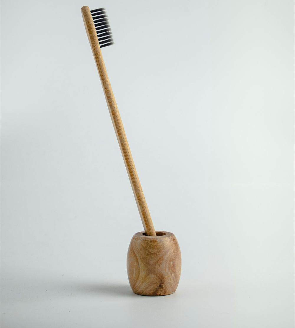 A bamboo toothbrush standing in a small wooden holder against a pale wall