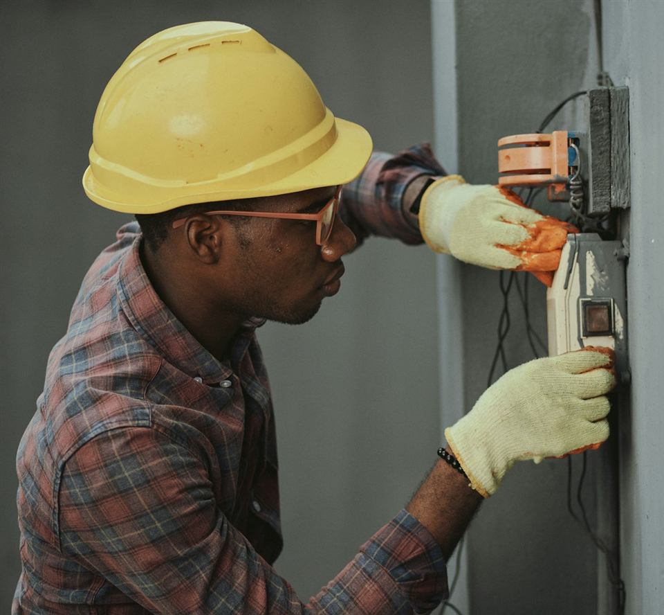 A Northstar electrician in a yellow hard hat and gloves fitting a meter to a wall
