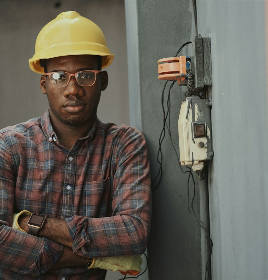 A Northstar electrician in a yellow hard hat, arms folded, standing beside a wall-mounted electrical box