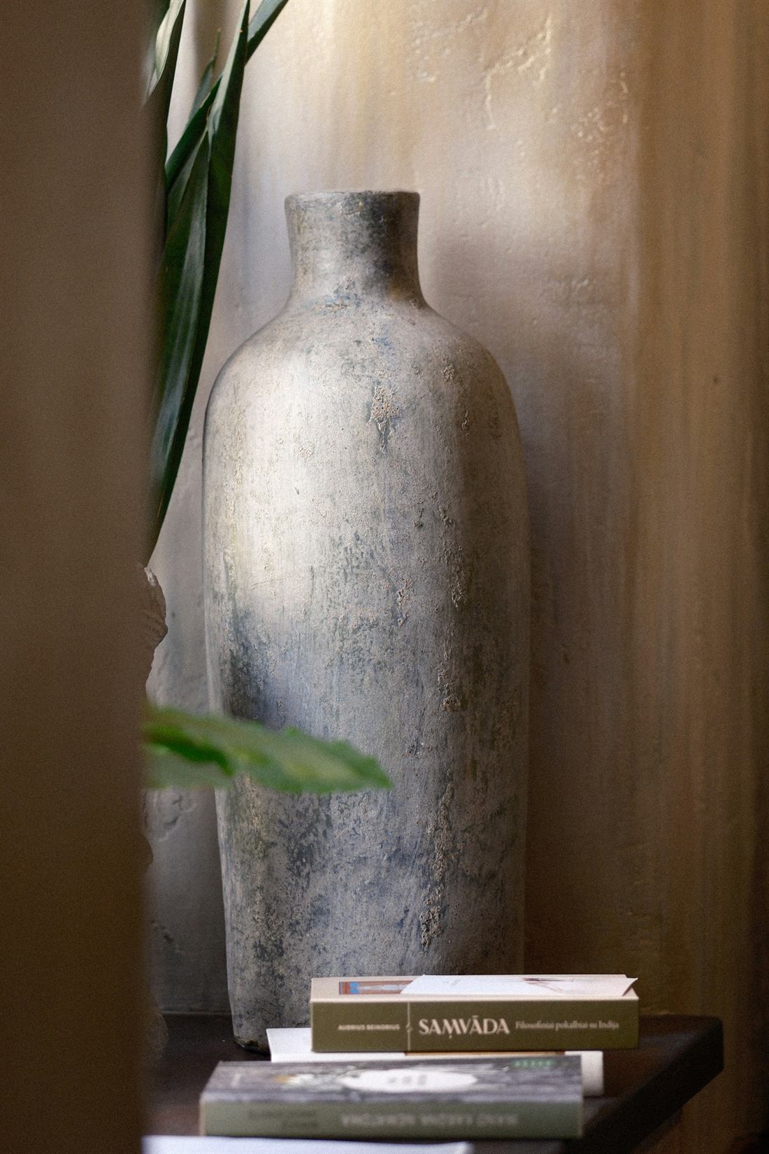 A textured stone vase and stacked books on a wooden shelf in soft window light